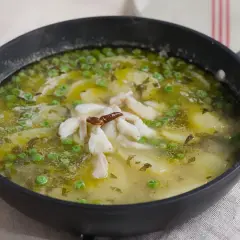 Patatas en salsa verde con trozos de pescado blanco y guisantes, servido en una sartén negra.