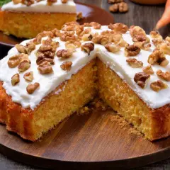 Un delicioso bizcocho de zanahoria, cubierto con glaseado blanco y nueces, servido en una tabla de madera.