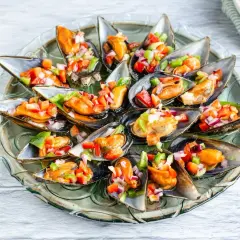 Mejillones a la vinagreta, frescos y coloridos, servidos en su concha con una picada de pimientos y cebolla.