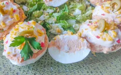 Deliciosos huevos rellenos adornados con aceitunas, perejil y trocitos de huevo duro, servidos sobre una cama de lechuga fresca.