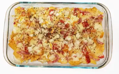 Nachos con queso horneados, cubiertos con trozos de tocino y pimientos rojos.
