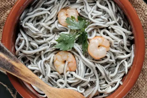 Deliciosas recetas con gulas y gambas, servidas en cazuela de barro con perejil y cuchara de madera.