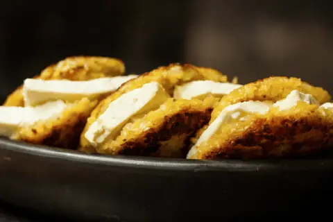 Arepas de choclo doradas y crujientes, rellenas de queso blanco fresco, servidas en un cuenco de barro.