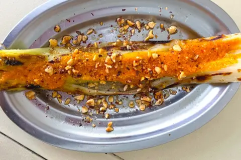 Puerros al horno con salsa picante y frutos secos picados, servidos en un plato metálico.