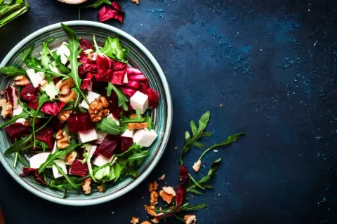 Ensalada de remolacha vibrante con queso feta, nueces y rúcula en un plato azul.