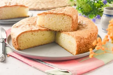 Bizcocho sin huevo esponjoso y dorado, servido en un plato gris con un cuchillo de plata. Perfecto para un postre ligero.
