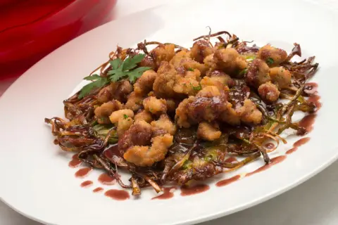 Mollejas de cordero rebozadas y crujientes, servidas sobre verduras salteadas y bañadas en una salsa oscura. ¡Una delicia para aprender como hacer mollejas de cordero!