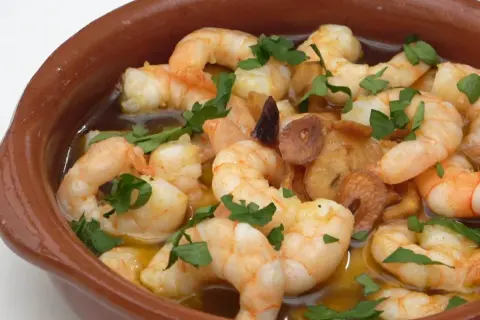 Gambas al pil pil burbujeantes en cazuela de barro, con ajo dorado y perejil fresco.