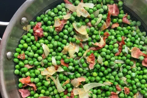 Guisantes con jamón y cebolla en una sartén. Un plato sencillo y sabroso, listo para disfrutar.