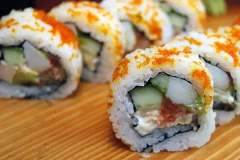 Rollos de sushi caseros con salmón, aguacate y pepino, cubiertos de tobiko. ¡Una guía fácil de como hacer sushi en casa!