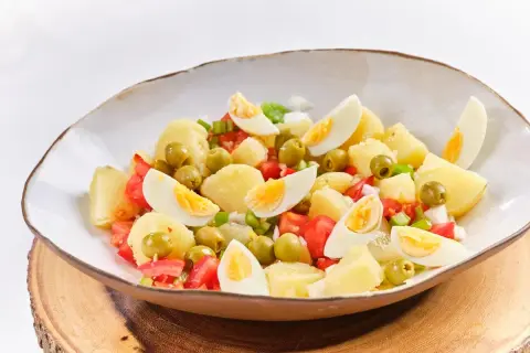 Ensalada campera con patatas, huevos cocidos, tomates y aceitunas verdes, servida en un cuenco rústico.