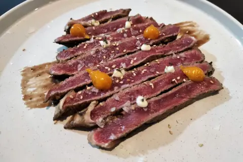 Tataki de ternera, finas lonchas de carne rosada con sésamo, sal gorda y toques de salsa y puré de mango.