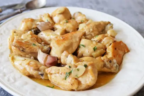 Sabroso pollo al ajillo servido en un plato blanco, con trozos de pollo dorados y jugosos, cubiertos con una salsa de ajo y perejil.