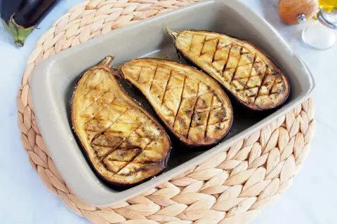 Berenjenas asadas al horno, cortadas por la mitad y con un patrón de rejilla, listas para disfrutar.
