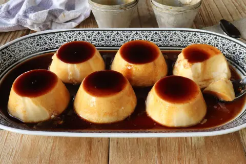 Seis deliciosos flanes de leche condensada, bañados en caramelo oscuro, servidos en una bandeja decorada.