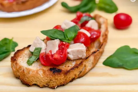 Una bruschetta que es un pan tostado cubierto con tomates frescos, cubos de mozzarella y hojas de albahaca verde.