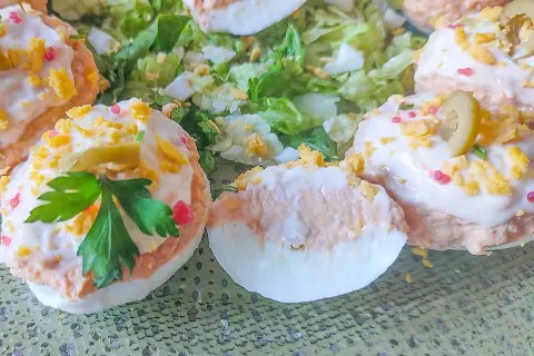 Deliciosos huevos rellenos adornados con aceitunas, perejil y trocitos de huevo duro, servidos sobre una cama de lechuga fresca.