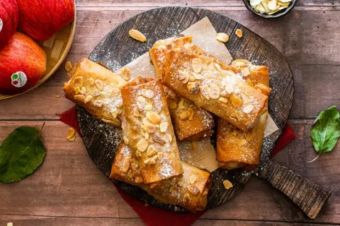 Deliciosos rollos de strudel de manzana dorados, espolvoreados con azúcar glas y almendras fileteadas, listos para disfrutar.