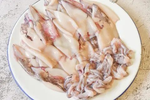 Plato con chipirones limpios y tentáculos listos para freír. Se aprecian sus manchas oscuras y tonos rosados.