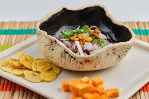 Delicioso ceviche de corvina en cuenco rústico, acompañado de patacones y cubos de camote.