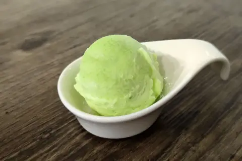 Una bola de helado de manzana verde en un cuenco blanco sobre una mesa de madera.