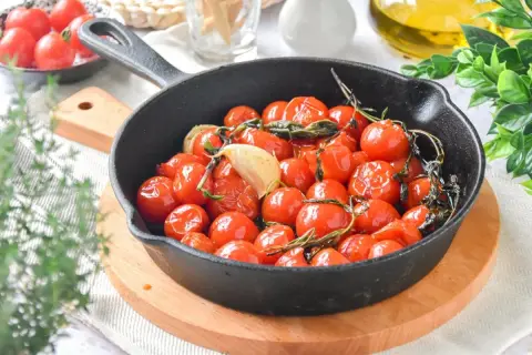 Tomates cherry confitados en sartén de hierro fundido con ajo y hierbas. Un plato delicioso y aromático.