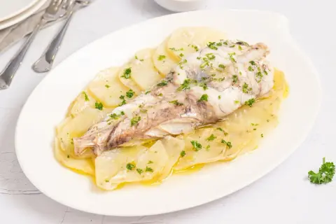 Delicioso rape al horno sobre cama de patatas laminadas, espolvoreado con perejil fresco.