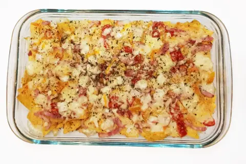 Nachos con queso horneados, cubiertos con trozos de tocino y pimientos rojos.