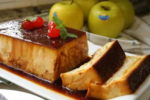 Delicioso pudin de manzana con caramelo, decorado con cerezas y menta. Manzanas verdes al fondo.