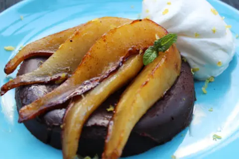 Deliciosa marquesa de chocolate con peras caramelizadas y crema batida, adornada con menta y ralladura de limón.
