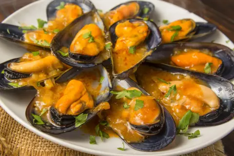 Mejillones en salsa, como los de los bares, servidos en una cazuela blanca con perejil picado.