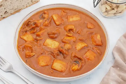 Un plato humeante de jibia en salsa, con trozos de patata y pan rústico al lado.