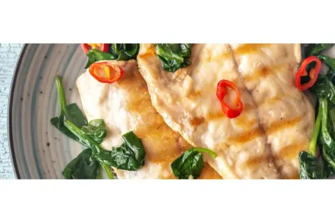 Dorada a la plancha con espinacas y rodajas de chile rojo, servida en un plato azul y blanco.
