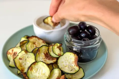 Crujientes rodajas de calabacín en airfryer, servidas con aceitunas negras y una salsa para mojar.