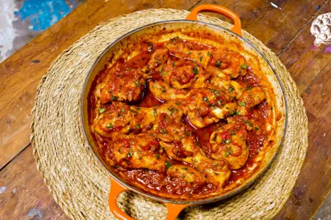 Pollo a la toledana en cazuela naranja, servido sobre una esterilla de mimbre en una mesa de madera rústica.