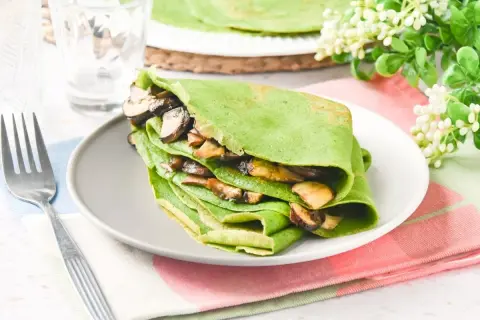 Deliciosos crepes de espinacas rellenos de champiñones salteados, servidos en un plato gris con un tenedor al lado.