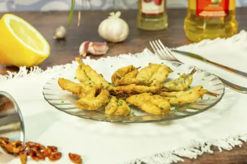 Un plato de boquerones en adobo crujientes, servidos con limón, ajo y guindillas.