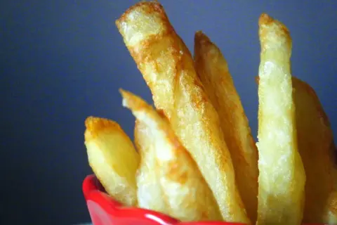 Patatas fritas doradas y crujientes en un recipiente rojo.