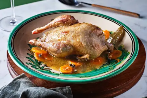 Perdiz a la toledana servida en plato decorado con rodajas de zanahoria y especias.