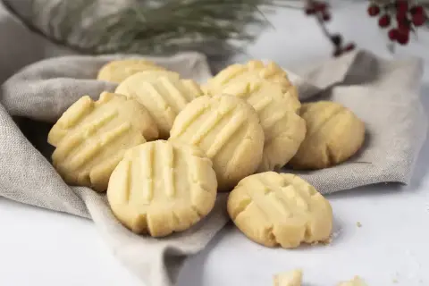 Montón de galletas de mantequilla doradas con líneas marcadas, servidas sobre una tela gris.