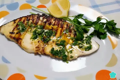 Delicioso emperador a la plancha con perejil fresco, ajo y limón, servido en un plato blanco con círculos de colores.