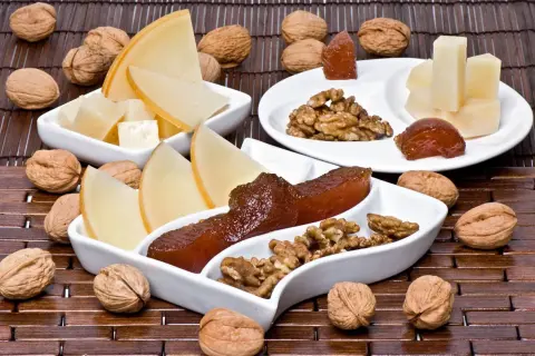 Queso y nueces acompañan trozos de dulce de manzana en una tabla de madera.
