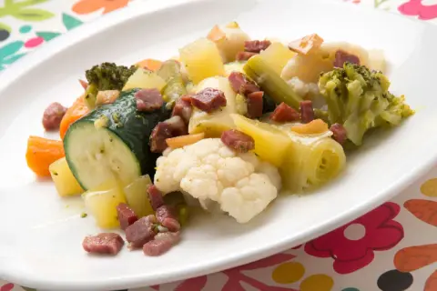 Un colorido panache de verduras con brócoli, coliflor, calabacín, zanahoria y patatas, salpicado de trocitos de jamón.