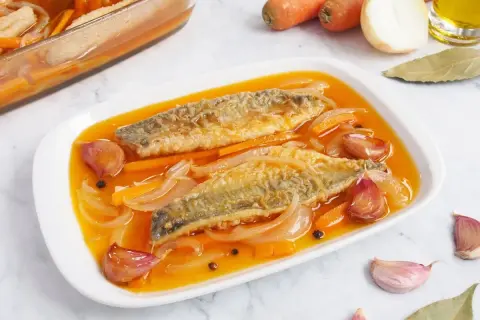 Dos filetes de caballa en escabeche, con zanahoria, cebolla y ajos en una salsa dorada.