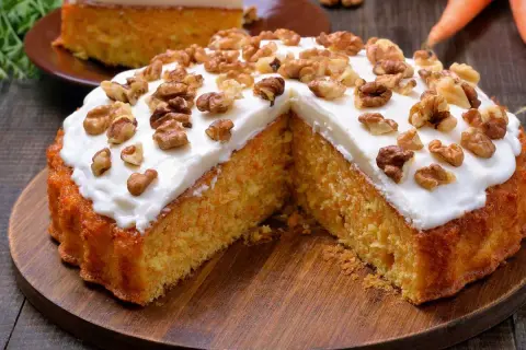 Un delicioso bizcocho de zanahoria, cubierto con glaseado blanco y nueces, servido en una tabla de madera.