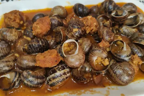 Un plato abundante de caracoles en salsa, con trozos de chorizo y especias, listo para disfrutar.