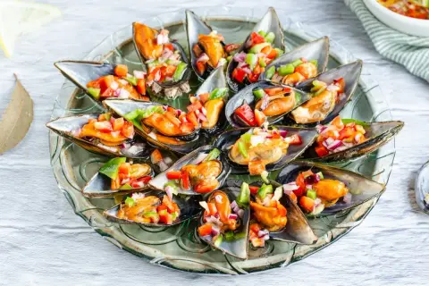 Mejillones a la vinagreta, frescos y coloridos, servidos en su concha con una picada de pimientos y cebolla.
