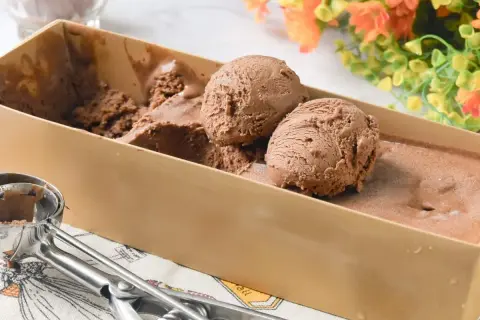 Dos bolas de helado de chocolate casero recién servidas en un recipiente, con una cuchara para helado al lado.