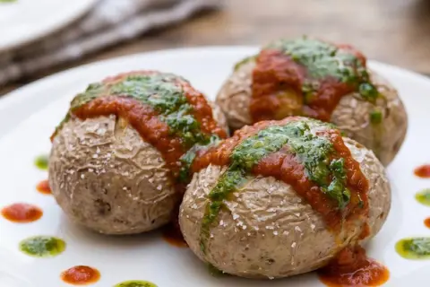 Tres papas arrugadas con mojo rojo y verde, sal marina y puntos de salsa en un plato blanco.