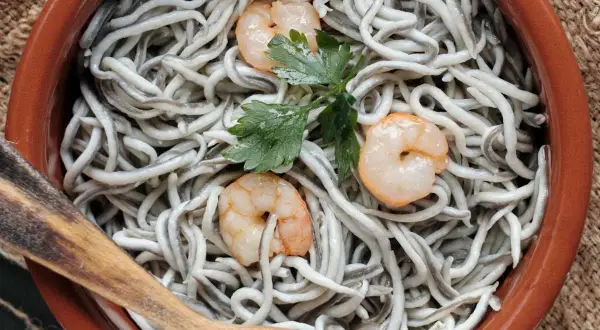 Deliciosas recetas con gulas y gambas, servidas en cazuela de barro con perejil y cuchara de madera.